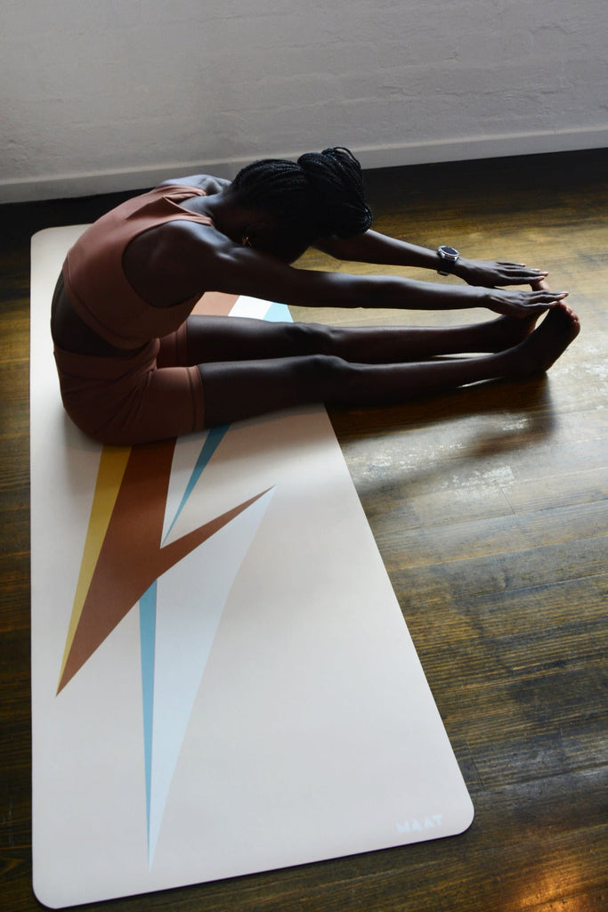 Girl sitting and bending forwards on the mat with two hands touching toes